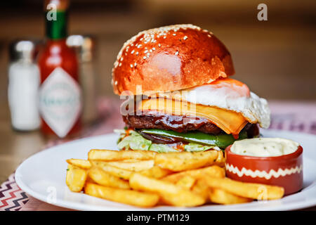 Appena cucinato hamburger fatti in casa con carne di manzo macinata, il formaggio cheddar e uovo fritto con patate fritte e erbe fresche Foto Stock