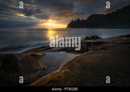 Tugeneset costa rocciosa con le montagne sullo sfondo al tramonto, Senja, Norvegia Foto Stock