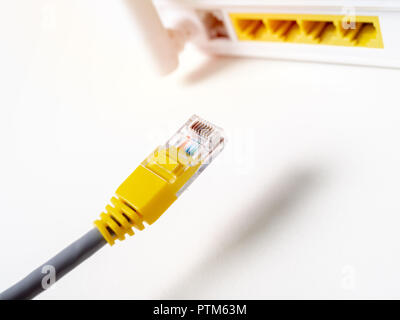 Close-up cavo ethernet giallo che collega il bianco internet wireless router WI-FI hub di rete isolato su sfondo bianco con copia spazio. Foto Stock