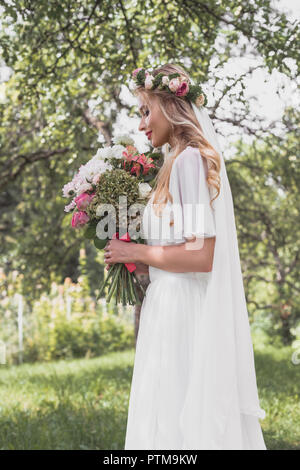 Vista laterale di sorridere giovane sposa azienda Bouquet nozze in posizione di parcheggio Foto Stock