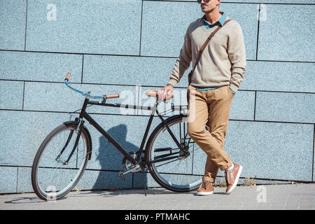 Ritagliato colpo di elegante uomo di mezza età in piedi con la bicicletta su strada Foto Stock