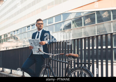 Imprenditore di successo in abbigliamento formale quotidiano di contenimento e guardando lontano mentre in piedi con la bicicletta su strada Foto Stock