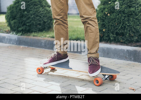 Ritagliato colpo di uomo in piedi su longboard su strada Foto Stock