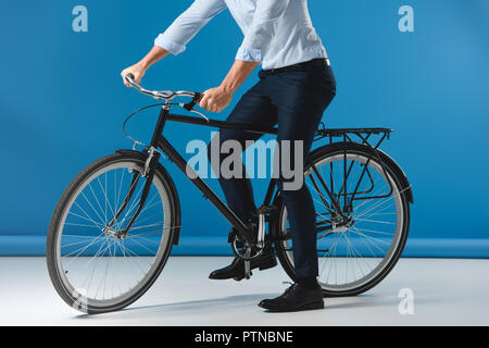 Ritagliato colpo di elegante uomo seduto sulla bicicletta su blu Foto Stock