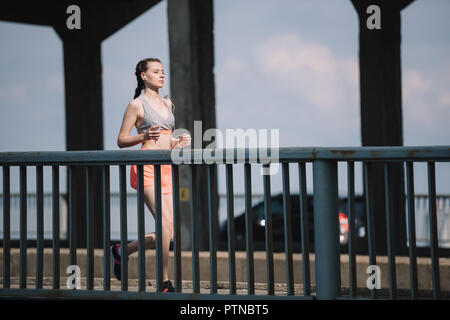 Pareggiatore femmina ascoltando musica e in esecuzione sul ponte in città Foto Stock