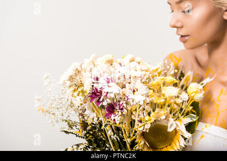 Donna attraente con bouquet di fiori e di vernice gialla sul corpo isolato su bianco Foto Stock
