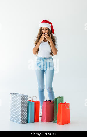 Sorpreso la ragazza di santa hat guardando le borse della spesa, isolato su bianco Foto Stock