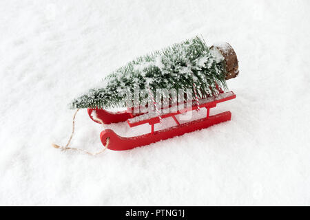 Primo piano di un legno rosso slitta nella neve portante un Natale abete. Foto Stock