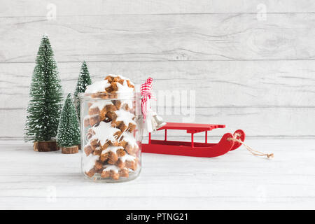 Biscotti di Natale in un vaso di vetro con decorazione di Natale e una slitta miniatura abeti in background. Foto Stock