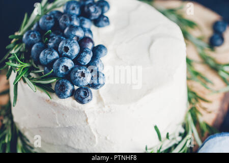 Bianco panna torta con belle decorazioni in inverno con mirtilli freschi e rosmarino su una tavola di legno di verri. Vista da sopra. Foto Stock