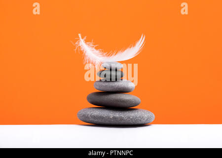 La meditazione di pietre e plume isolato sul colore di sfondo. Concetto di pesante e leggero. Foto Stock