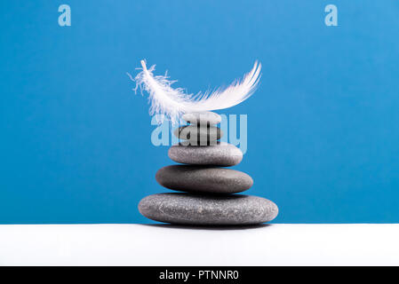 La meditazione di pietre e plume isolato sul colore di sfondo. Concetto di pesante e leggero. Foto Stock