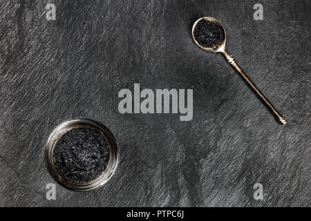 Una foto aerea del caviale nero in un vaso e in un cucchiaio, ripresa dall'alto su uno sfondo nero con copyspace Foto Stock