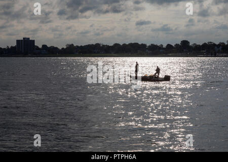 Detroit, Michigan - due uomini la pesca da una piccola barca sul Fiume Detroit. Windsor, Ontario, Canada si trova sul lato più lontano. Foto Stock