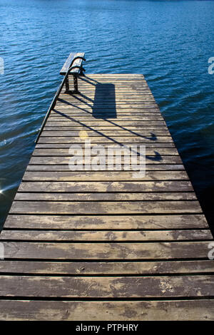 Bella molo in legno con panca e sun riflette sulla calma e acque blu, verticale Foto Stock