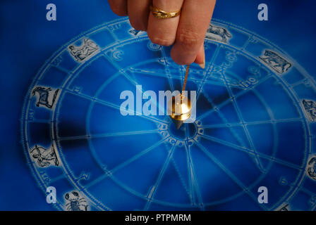 Mano che tiene un pendolo magico su una ruota dello zodiaco Foto Stock