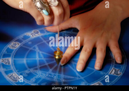 Mani con pendolo su una ruota dello zodiaco Foto Stock