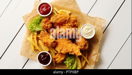 Salse e lattuga in prossimità di patatine fritte e di ali di pollo Foto Stock
