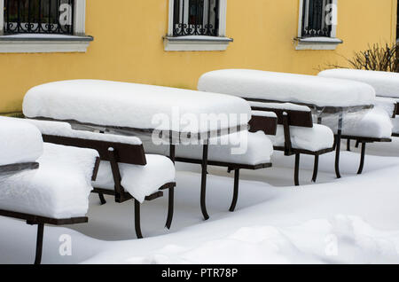 Tavoli in legno e panche di street cafe coperto con uno spesso strato di neve in inverno in bassa stagione Foto Stock