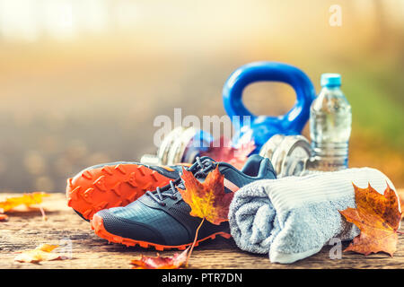 Coppia di blu scarpe di sport di acqua e manubri prevista su una tavola di legno in un albero autunno alley con foglie di acero - accessori per eseguire l'esercizio o worko Foto Stock