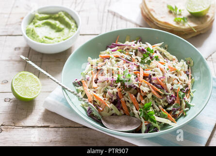 Coleslaw realizzato da verze, carote e varie erbe, servito con tortillas e guacamala su uno sfondo di legno. Messa a fuoco selettiva. Foto Stock