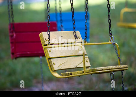 Close-up di legno vuota verniciata blu, giallo, sedili vintage sedie di multi-giostra colorati appesi su catene all'aperto in città parco divertimenti sull sunn Foto Stock