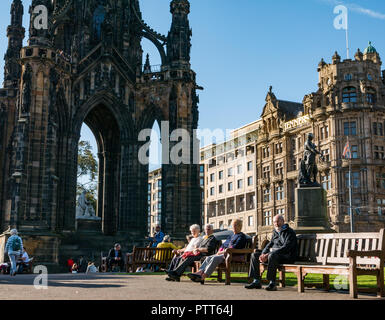 I giardini di Princes Street, Edimburgo, Scozia, Regno Unito, 10 ottobre 2018. Regno Unito: Meteo persone sedersi sulle panchine al sole accanto al monumento di Scott Foto Stock