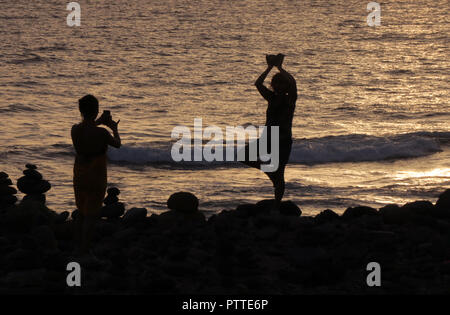 Due giovani donne in posa e fotografare ogni altro nel tramonto sul mare a Costa Adeje nel sud dell'Isola Canarie Tenerife, presa su 23.09.2018. Stoneworks artisticamente impilati con pietre naturali spesso servito come waymarkers nelle precedenti culture. Tuttavia le figure erette in luoghi eminenti non hanno più una tale funzione di oggi. Essi servono per escursionisti e turisti come espressione del loro attaccamento al luogo di identificazione con tradizioni e come simbolico stanziamento dell'ambiente, che conservazionisti di se stessi, tuttavia, criticare come un intervento indesiderato. | u Foto Stock