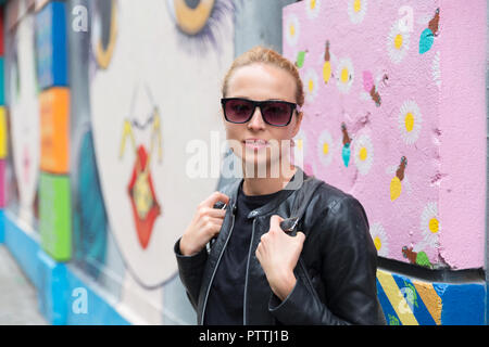 Donna che parla sullo smartphone appoggiata contro il coloratissimo graffito parete in New York City, Stati Uniti d'America. Foto Stock