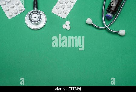 Lo stetoscopio e compresse di pillole isolata su uno sfondo verde, immagine concettuale Foto Stock