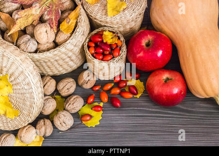 Noci mele rosse, rosa canina, zucca e foglie di giallo su una superficie in legno, cibo sano dalla natura. Concetto di sfondo di autunno Foto Stock