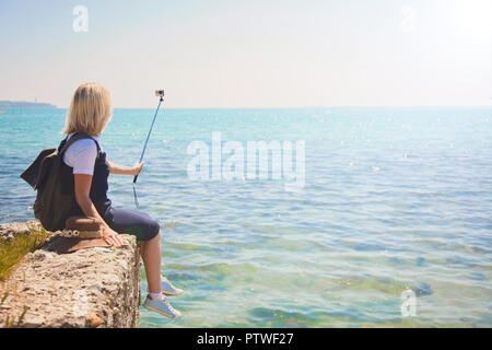 Piuttosto giovane turista prende selfie ritratto in riva al mare in una giornata di sole ragazza prende la foto per viaggi blog vista dal retro del turista travele Foto Stock