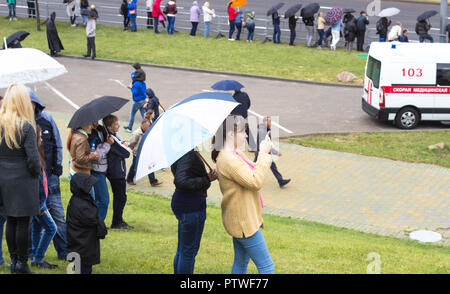 MINSK, Bielorussia - luglio 3, 2018: persone in piedi sulla strada con gli ombrelli sotto la pioggia, la bambina prende il largo sul telefono cellulare un incidente, un ambulanza Foto Stock
