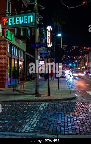 Tampa, FL--Ott 2, 2018; tempo esposizione di pedoni e automobili che viaggiano attraverso il red brick street di Ybor City sigaro storico quartiere del fattore di notte, Foto Stock