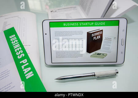 Business Guida di avvio su tablet o telefono cellulare con il business plan documenti e voglia di una penna per scrivere. Foto Stock