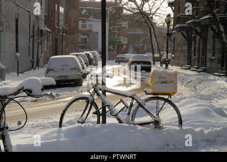 Inverno pieno di sole la mattina in Montreal, Canada : una bici attaccata ad un polo di segno sul marciapiede, accanto ad una piccola e coperta di neve street con macchine parcheggiate. Foto Stock