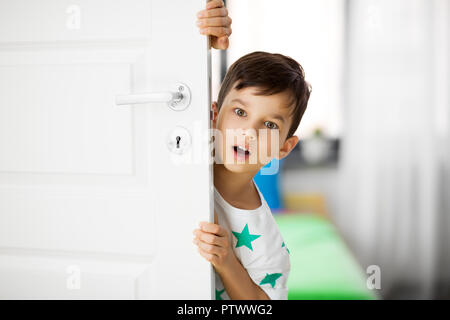Sorpreso little boy dietro la porta di casa Foto Stock