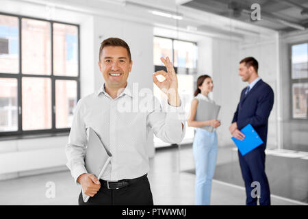 Agente immobiliare con cartella mostra segno OK con la mano in ufficio Foto Stock