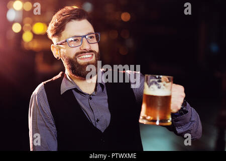 Carino giovane uomo attraente con un boccale di birra al pub sorridente e godersi la vita Foto Stock