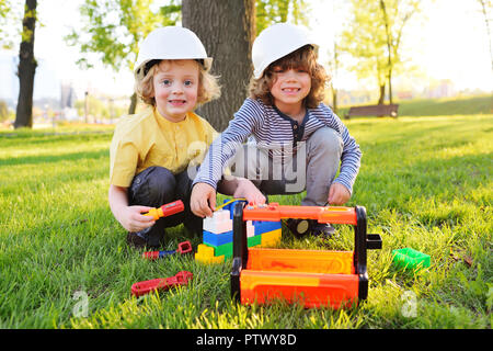 Due piccoli bambini carino nella costruzione di caschi in gioco dei lavoratori o dei costruttori con strumenti giocattolo in un parco sull'erba. Foto Stock