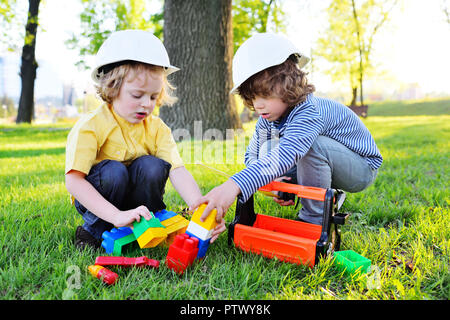 Due piccoli bambini carino nella costruzione di caschi in gioco dei lavoratori o dei costruttori con strumenti giocattolo in un parco sull'erba. Foto Stock