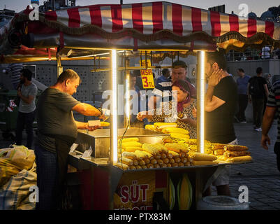 Istanbul, Turchia - 7 luglio 2018. Un venditore di stagionatura tutoli di mais in una bancarella di strada del quartiere Eminonu, un ex quartiere di Istanbul, Turchia, al tramonto. Foto Stock