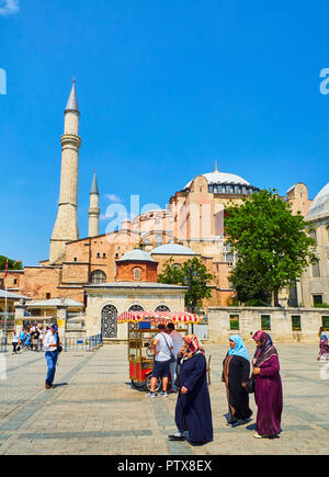 Istanbul, Turchia - 10 luglio 2018. Le donne musulmane e i turisti a piedi nella parte anteriore dell'Hagia Sophia mosque a luce solare e una di pannocchie di granoturco in stallo in avanti Foto Stock