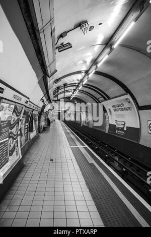 London Tube Station; Black & White shot della piattaforma deserta/ linea ferroviaria a London Marylebone stazione della metropolitana. Figura solitaria attende in distanza. Foto Stock