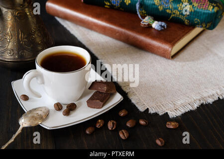 Tazzina di caffè nero con cucchiaino vintage, caffè turco di pentola e pezzetti di cioccolato sul legno scuro dello sfondo con il diario e il caso di matita Foto Stock