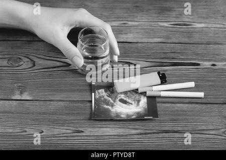 Una donna di mano trattiene un bicchiere di alcool, accanto ad essa è una fotografia della uzi gravidanza e sigarette, la gravidanza e il fumo di sigaretta, Foto Stock