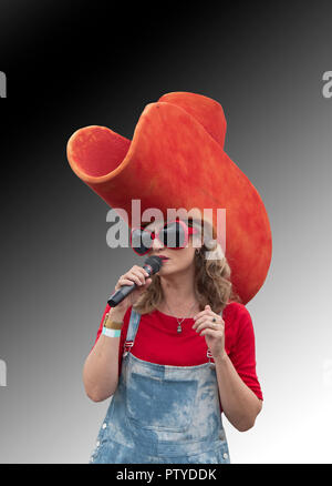 Ritratto di una bella cantante femminile tenendo un microfono e indossando un gigante di Red Hat ed enormi occhiali da sole rosso Foto Stock
