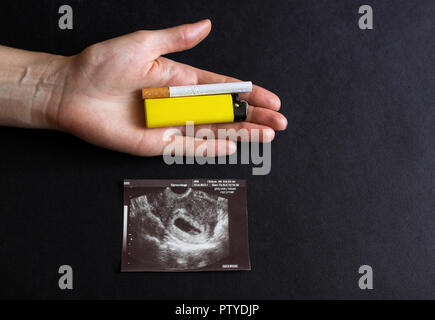 La futura madre detiene una sigaretta e un accendino in mano accanto a una fotografia della gravidanza uzi, gravidanza e il fumo, la gestazione Foto Stock