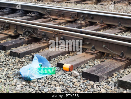 Un pacchetto con l'immondizia sulla ferrovia buttato fuori dalla finestra del treno da parte dei passeggeri, inquinamento, detriti e la stazione ferroviaria Foto Stock