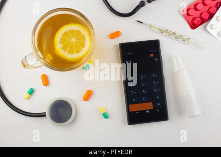 Tè con limone, termometro, pillole, telefono su sfondo bianco Foto Stock